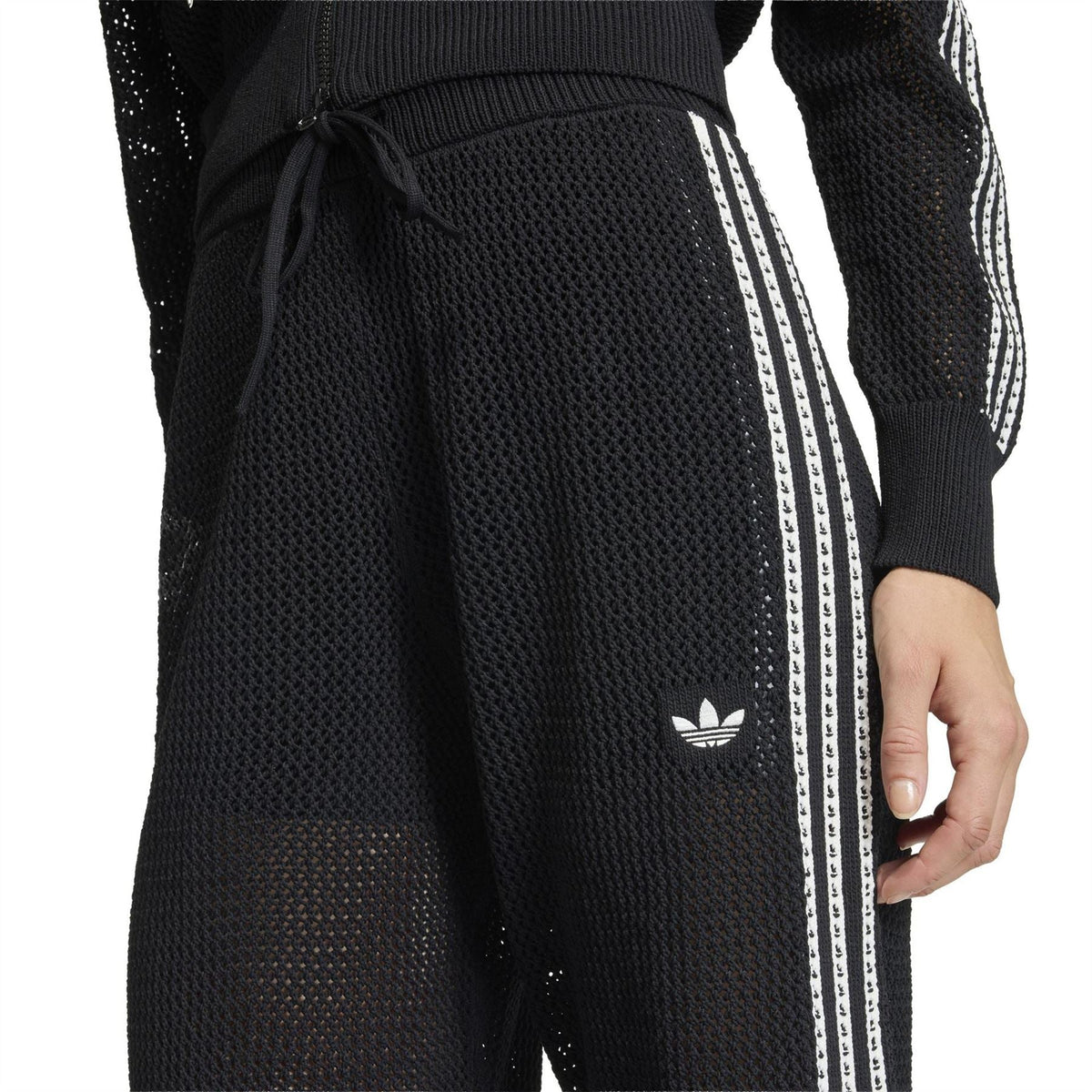 Close-up of black jersey joggers: drawstring waist, adidas trefoil, side stripe tape