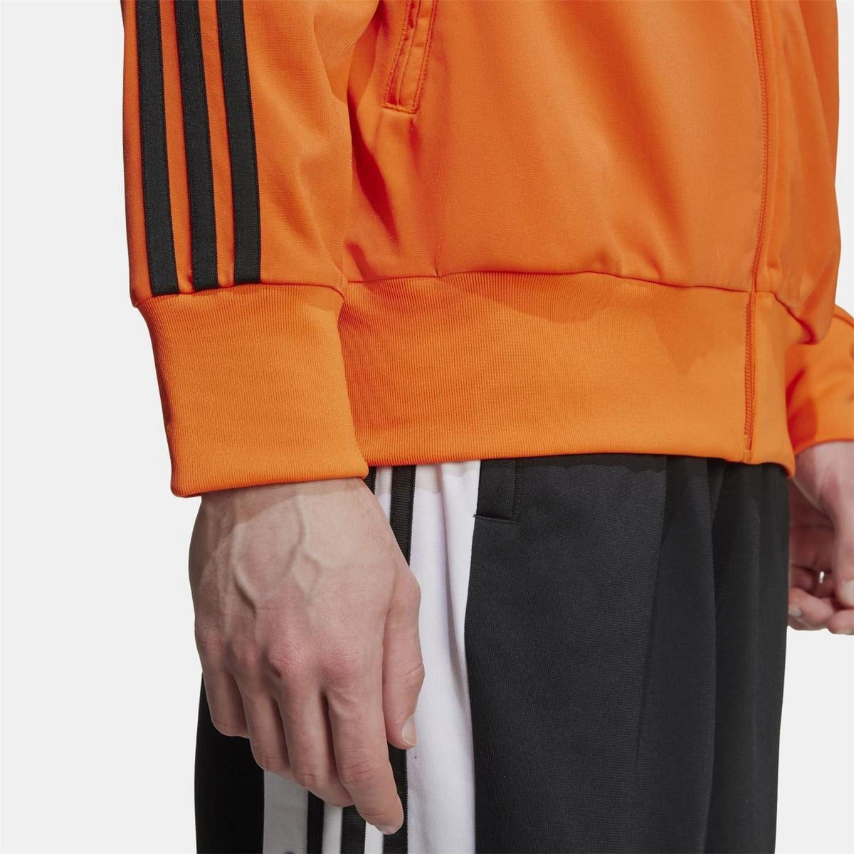 Orange track top detail with ribbed cuffs, black sleeve stripes, and zip front
