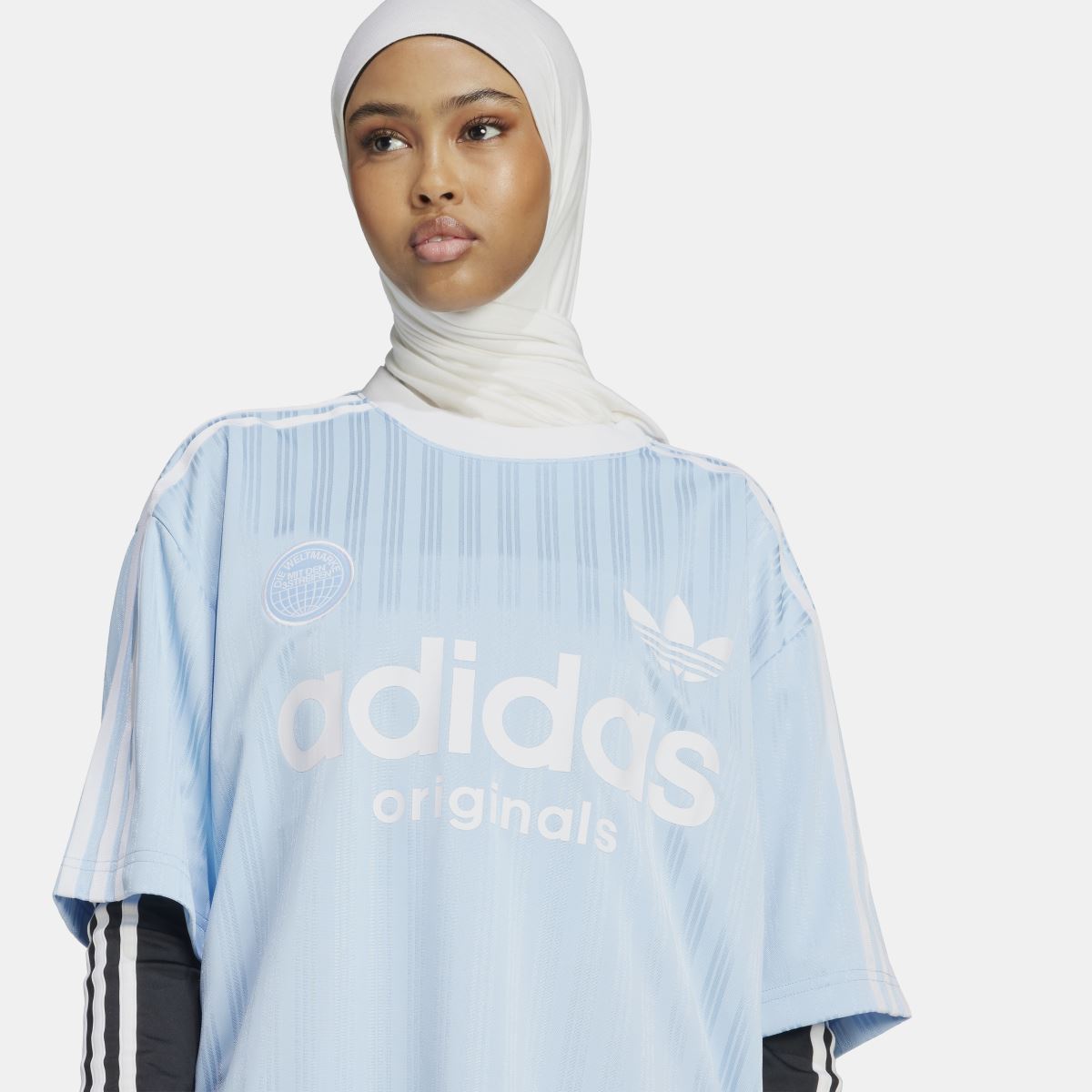 Light blue oversized t-shirt front view with adidas Originals logo and trefoil on striped fabric.