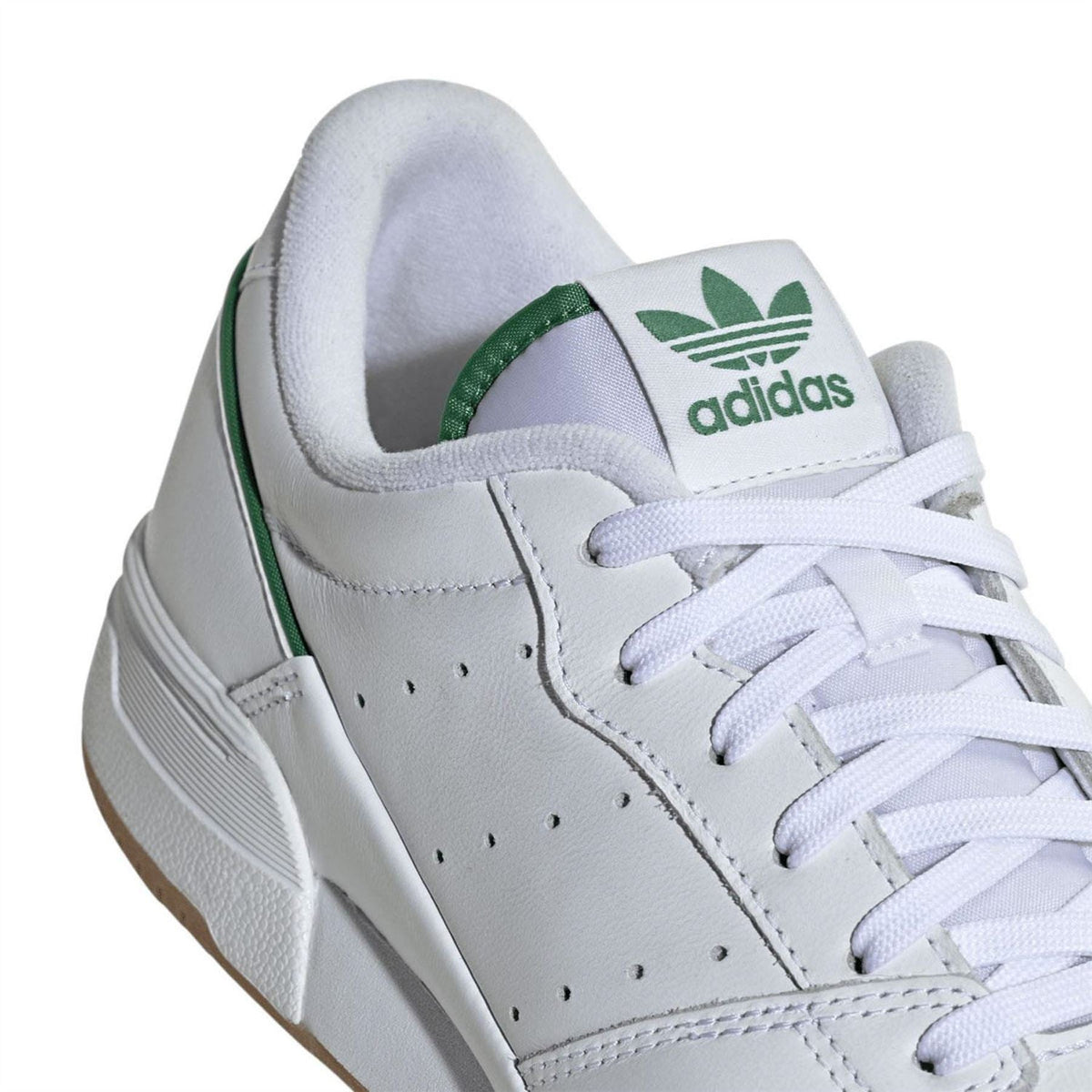 White leather trainer close-up with green heel lining and adidas logo