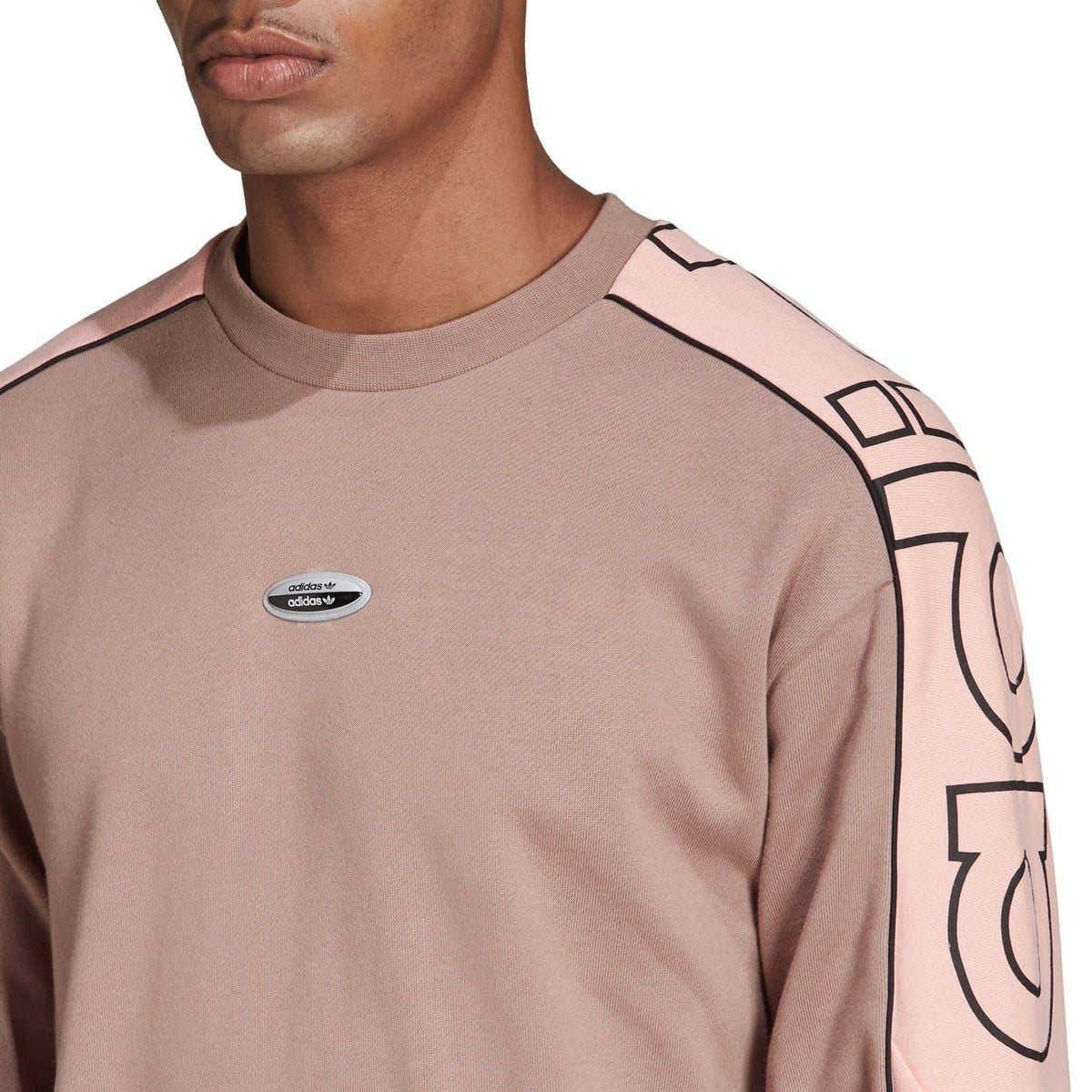 Close-up of chalky brown crewneck sweatshirt with adidas oval chest logo and pink trim