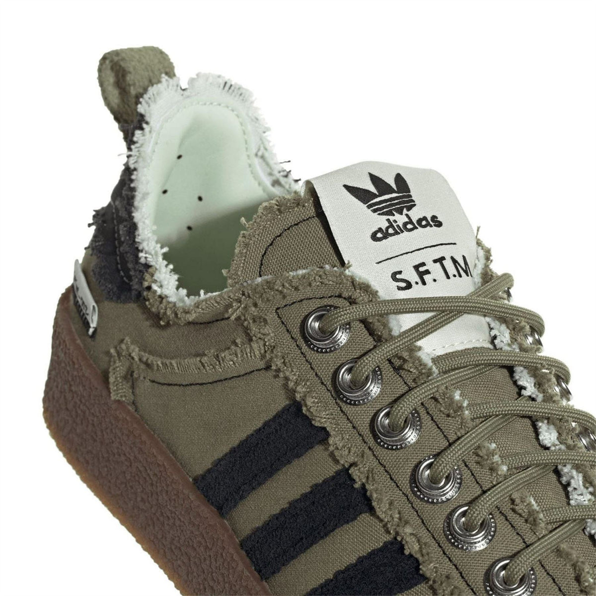 Close-up of olive trainers with adidas tongue tab, metal eyelets, and brown outsole
