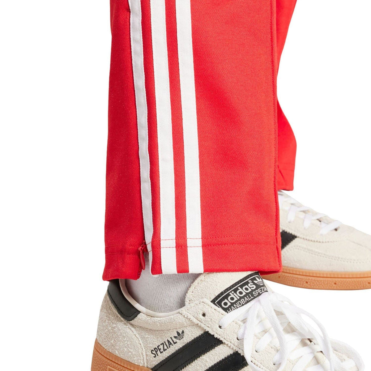 Red adidas track pants hem with white side stripes and elastic cuffs; sneakers visible.