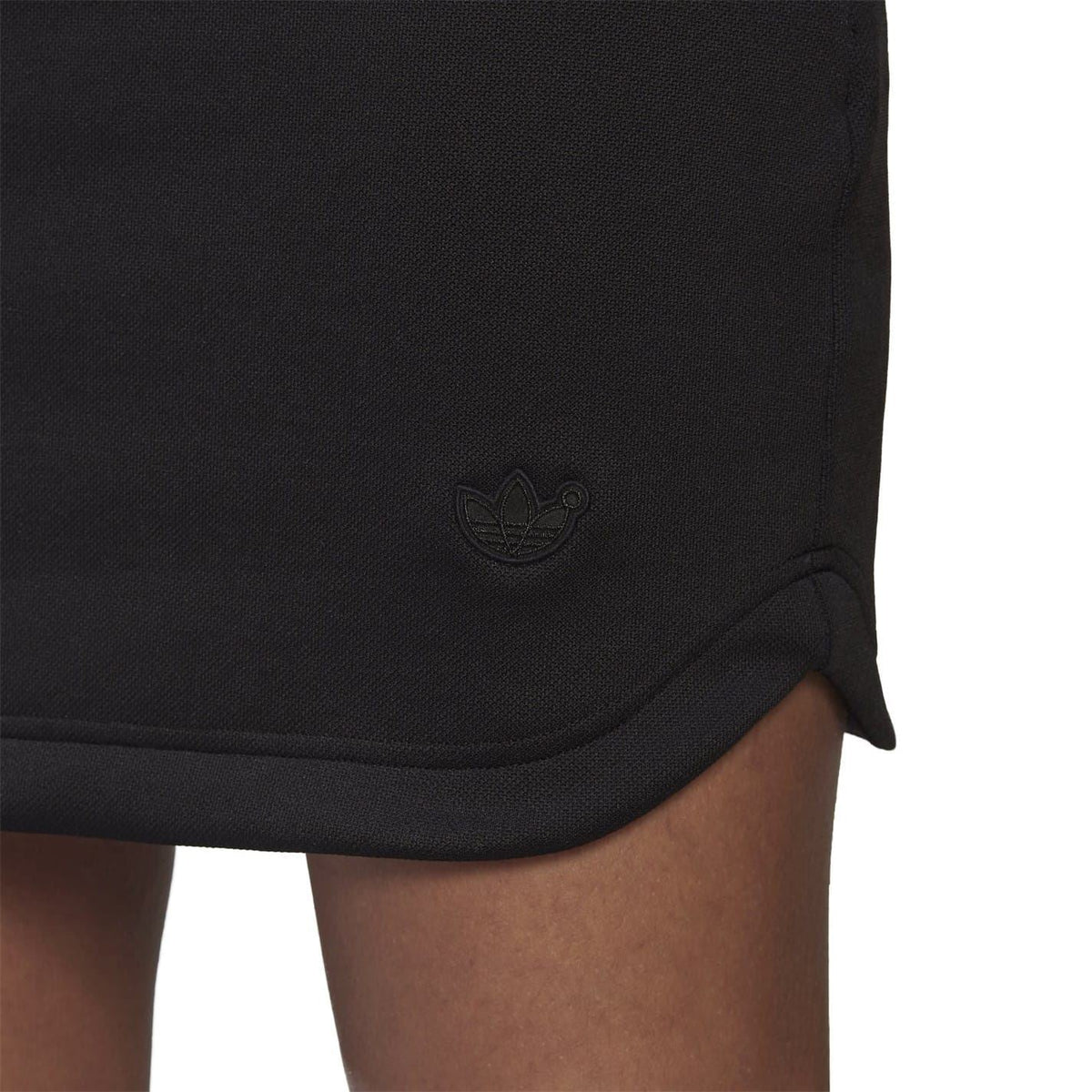 Black mini dress hem close-up with adidas trefoil logo on the skirt.