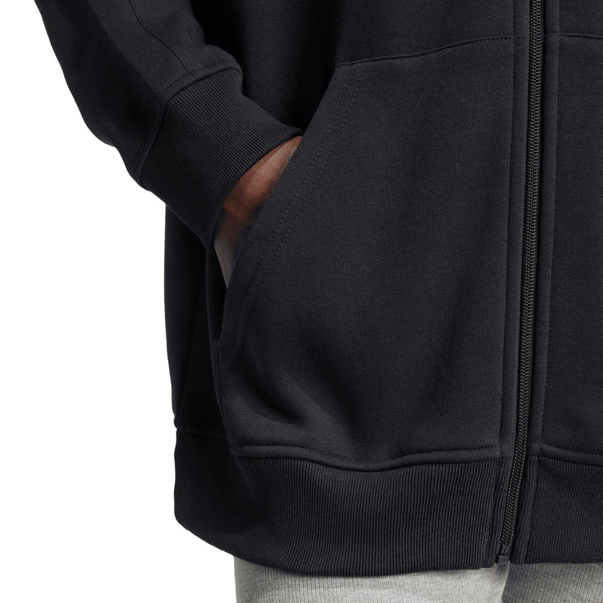 Black full-zip hoodie close-up of ribbed cuff, zipper, and front pocket seam