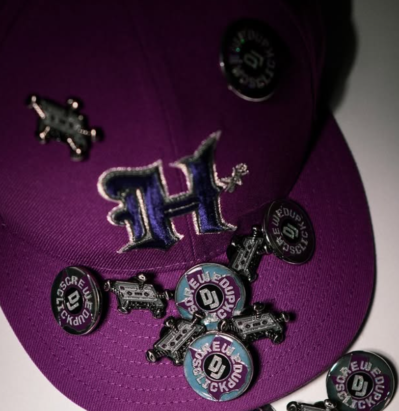 Purple baseball cap with multiple round pin badges and an embroidered H logo