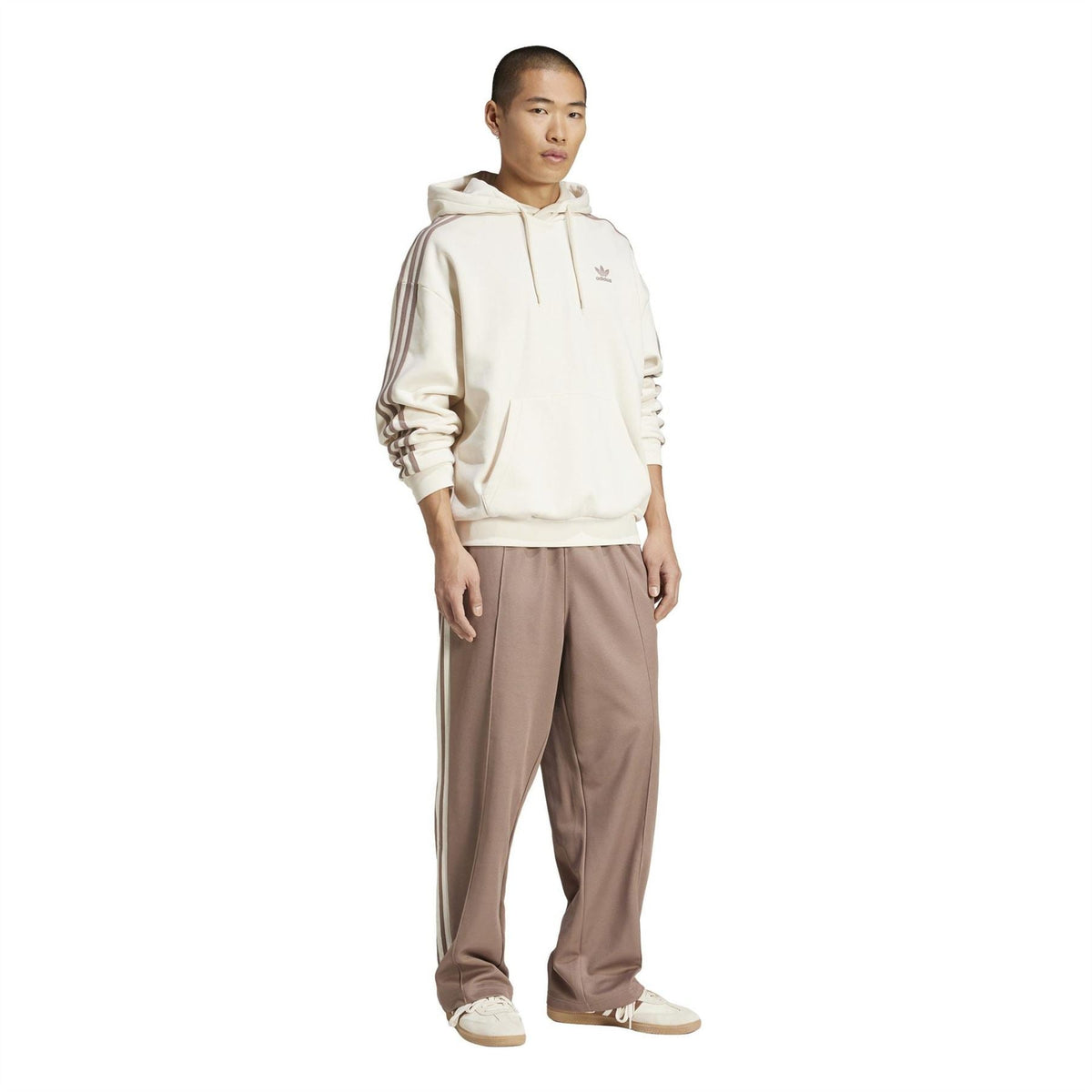 Off-white adidas Originals baggy hoodie with hood and three stripe sleeves, worn with joggers.