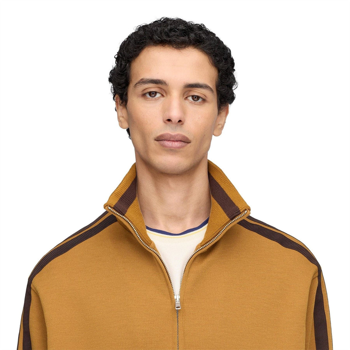 Tan track jacket close-up with stand collar, dark stripe trim, and logo label near zipper.