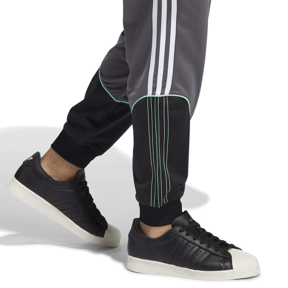 Grey track sweatpants worn with black sneakers; ribbed cuffs and green-striped detail