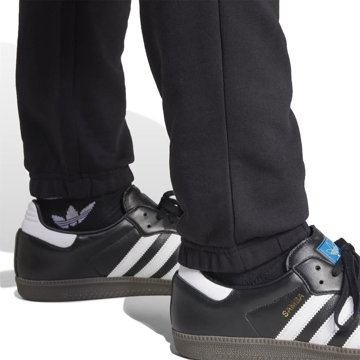 Black jogger cuffs gathered at ankle, paired with black adidas sneakers and striped detail