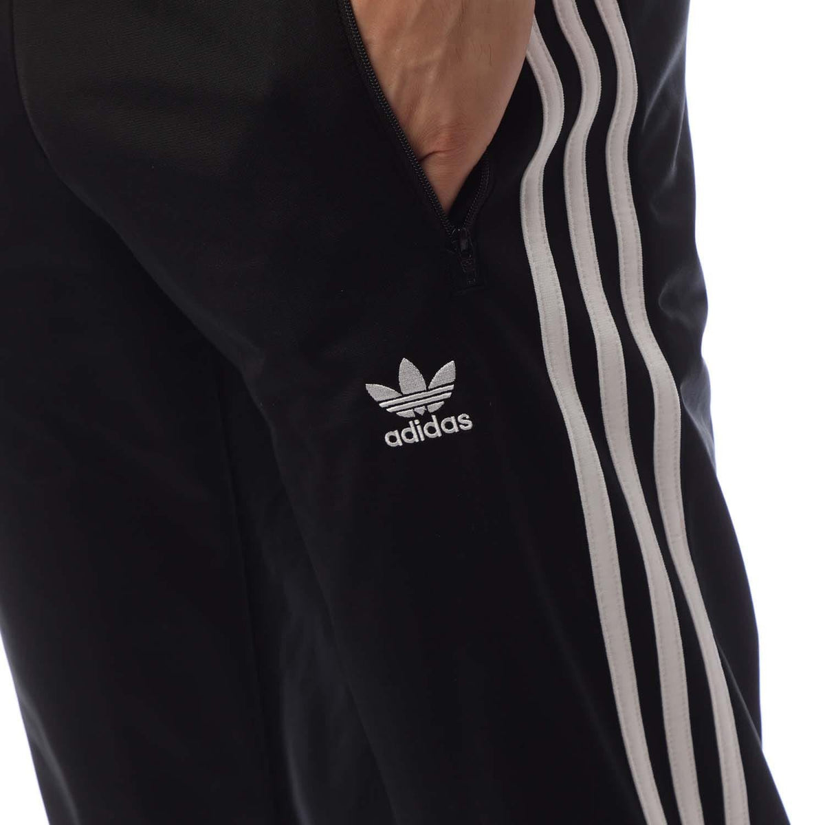 Close-up of Adidas trefoil logo on black track pants with white side stripes