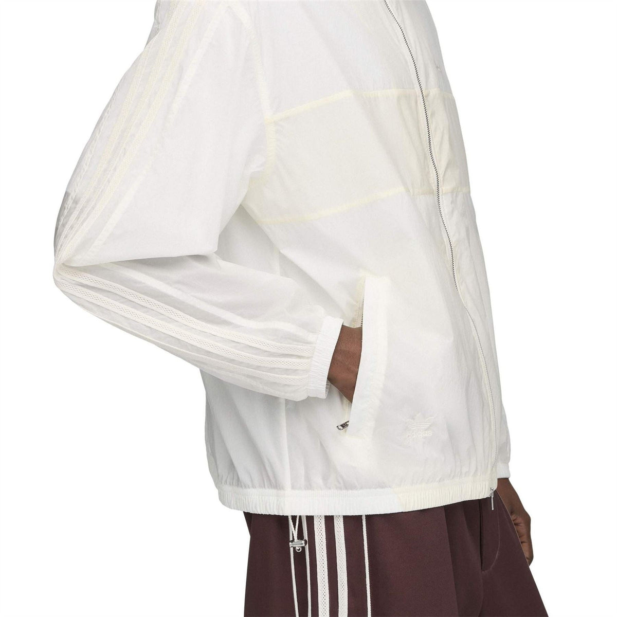 Chalk white track jacket side view with elastic cuffs, partial zip, and paneled design.