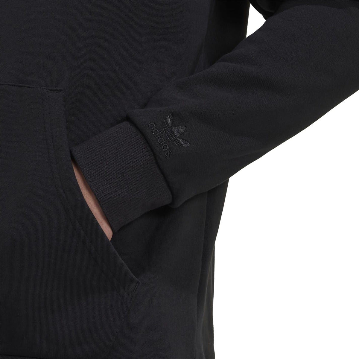Black sweatshirt sleeve cuff close-up with small embroidered trefoil logo.