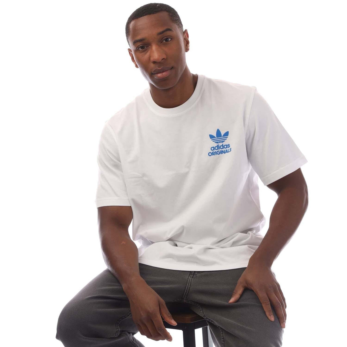 White adidas Originals short-sleeve T-shirt with blue chest logo, model seated