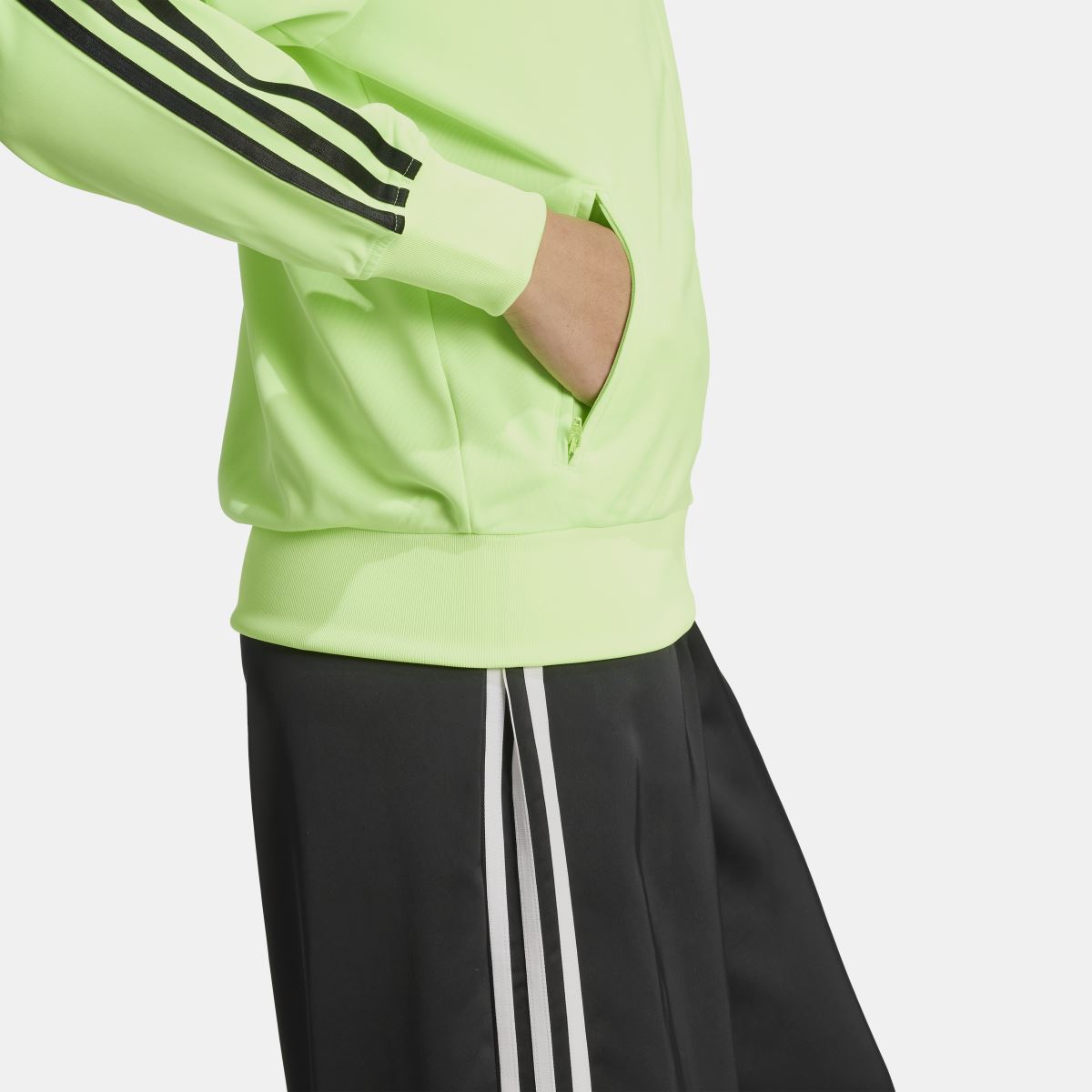Lime green track top showing ribbed hem and black three-stripe sleeve detail
