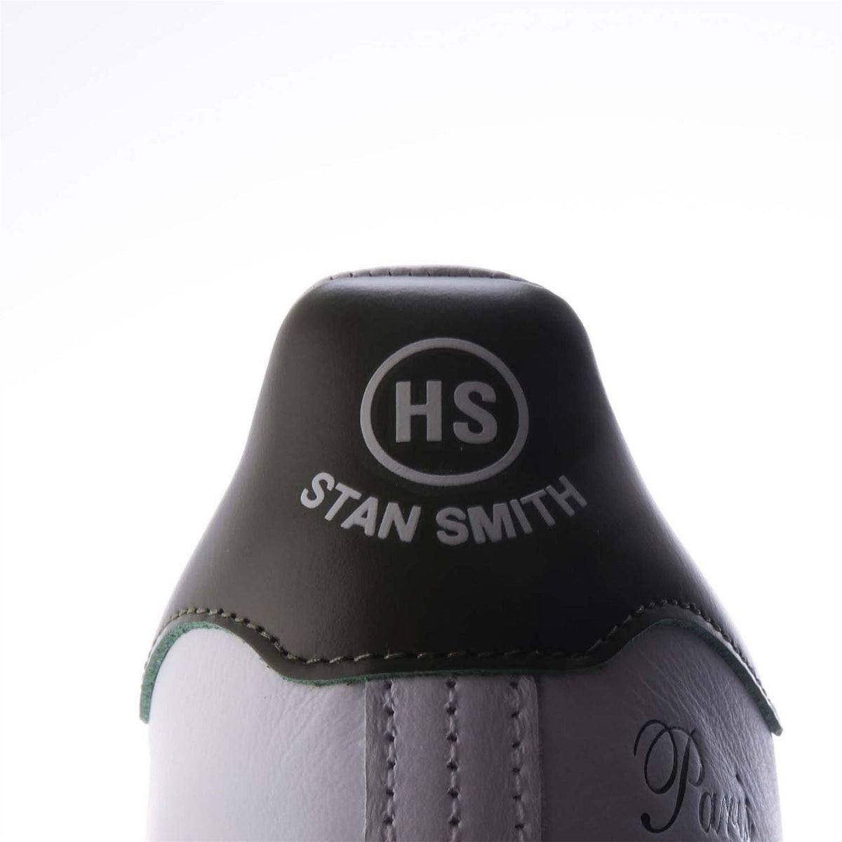 White sneaker with black heel patch showing HS and “Stan Smith” text.