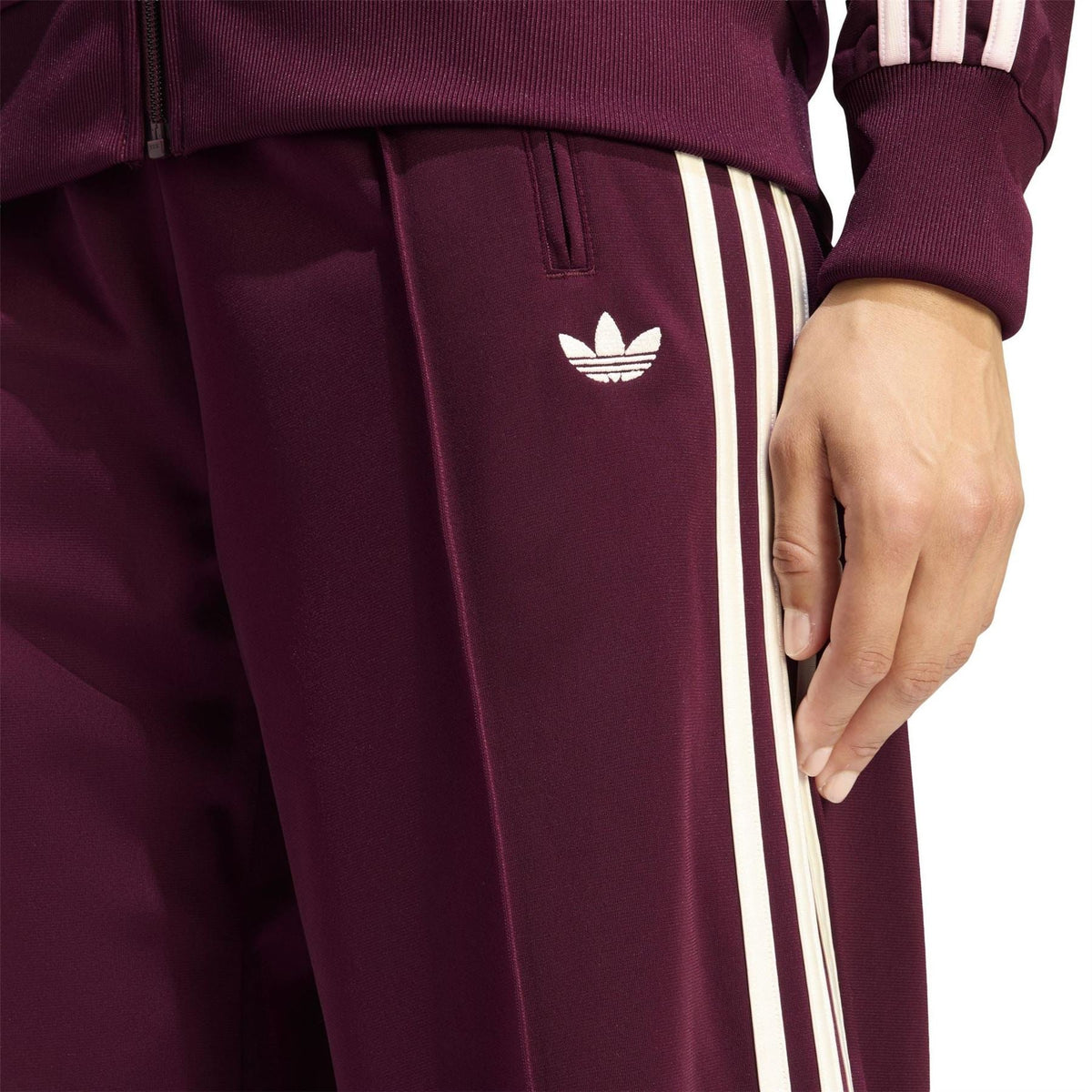 Maroon track pants with white triple stripe trim and small Adidas trefoil on thigh