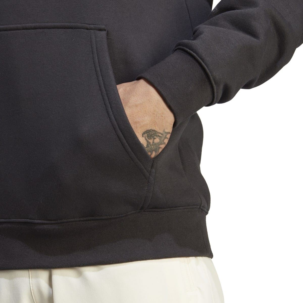 Black hoodie close-up of kangaroo pocket and ribbed cuff, partial tattoo visible