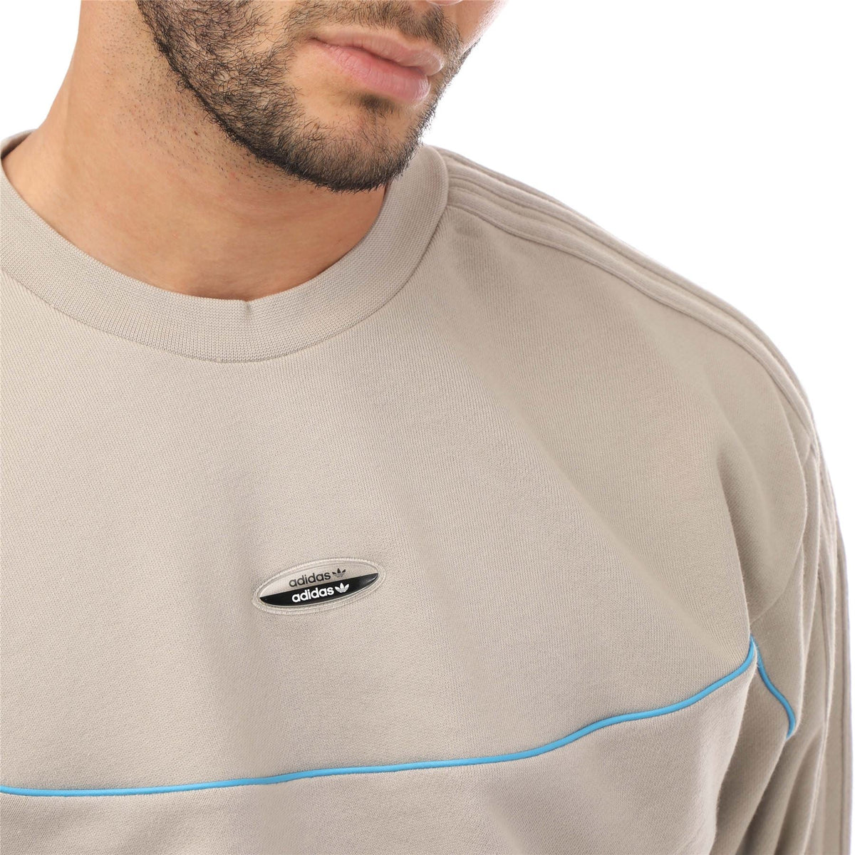 Light beige crewneck sweatshirt close-up with adidas logo patch and blue contrast stripe