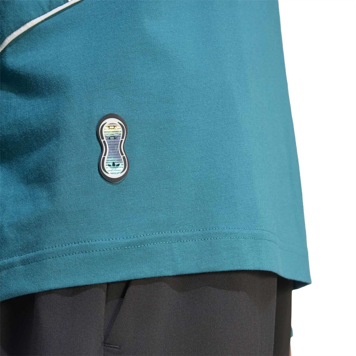 Teal jersey T-shirt hem patch with small stitched graphic and white seam detail