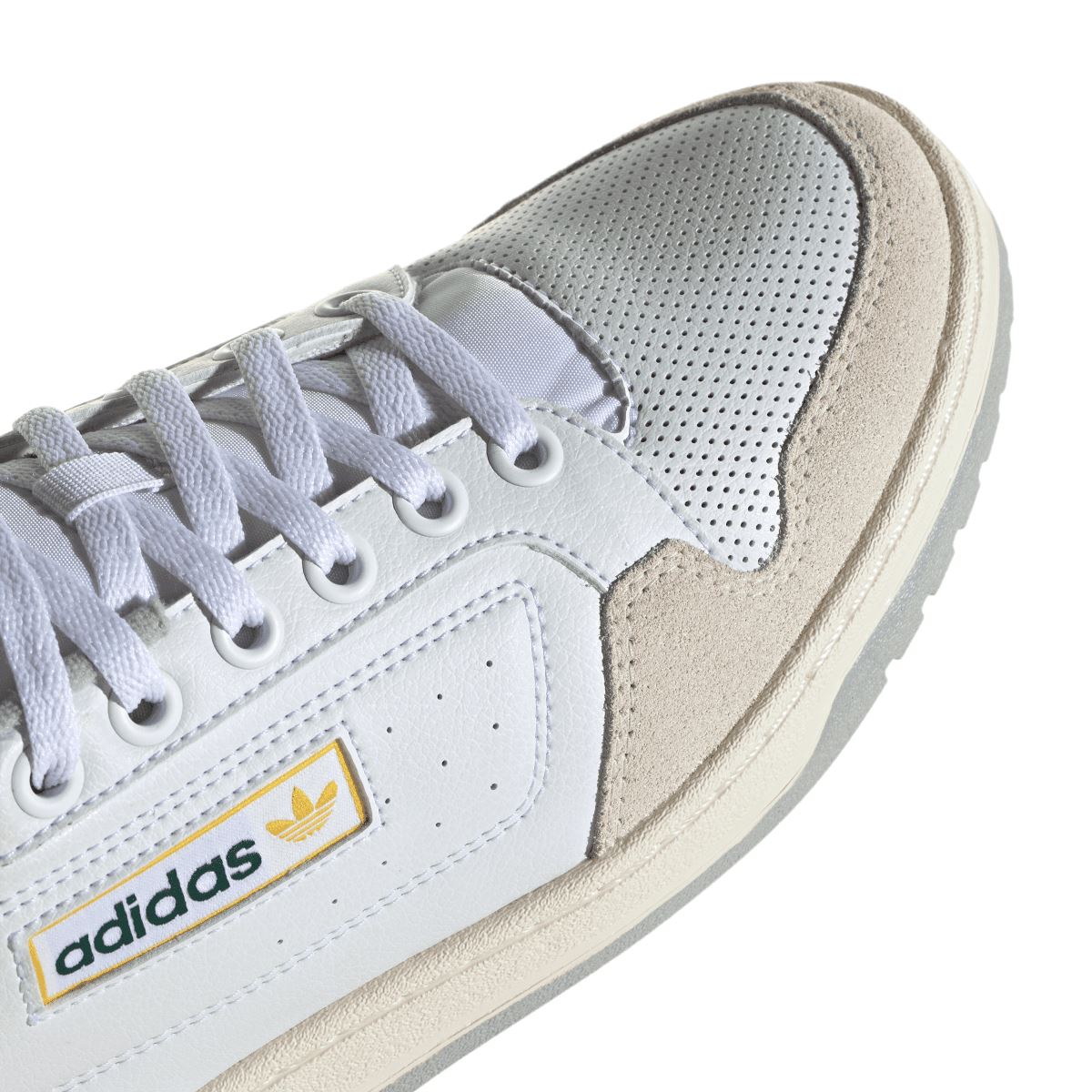 Close-up of white adidas NY 90 shoe with perforations, lace, and yellow logo patch