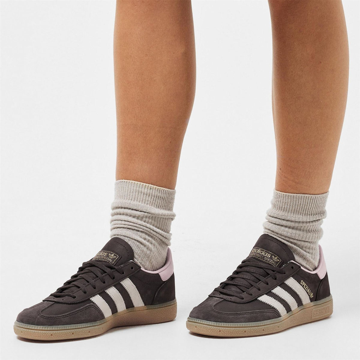 Pair of brown adidas Spezial sneakers on model feet with light gray socks.