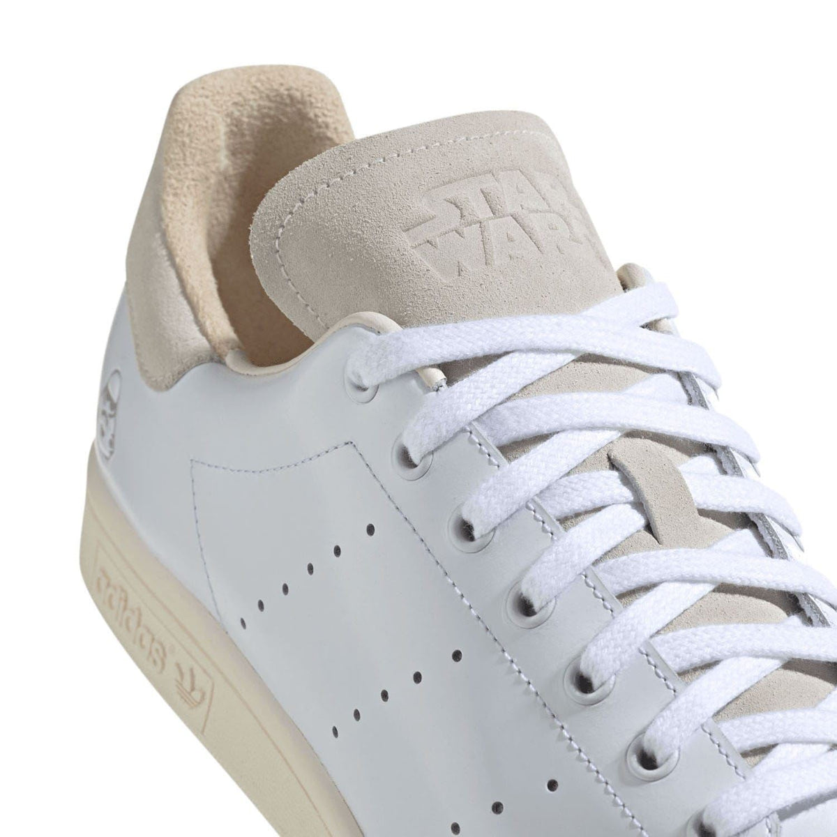 Close-up of white leather-look upper with perforated toe and beige suede lining