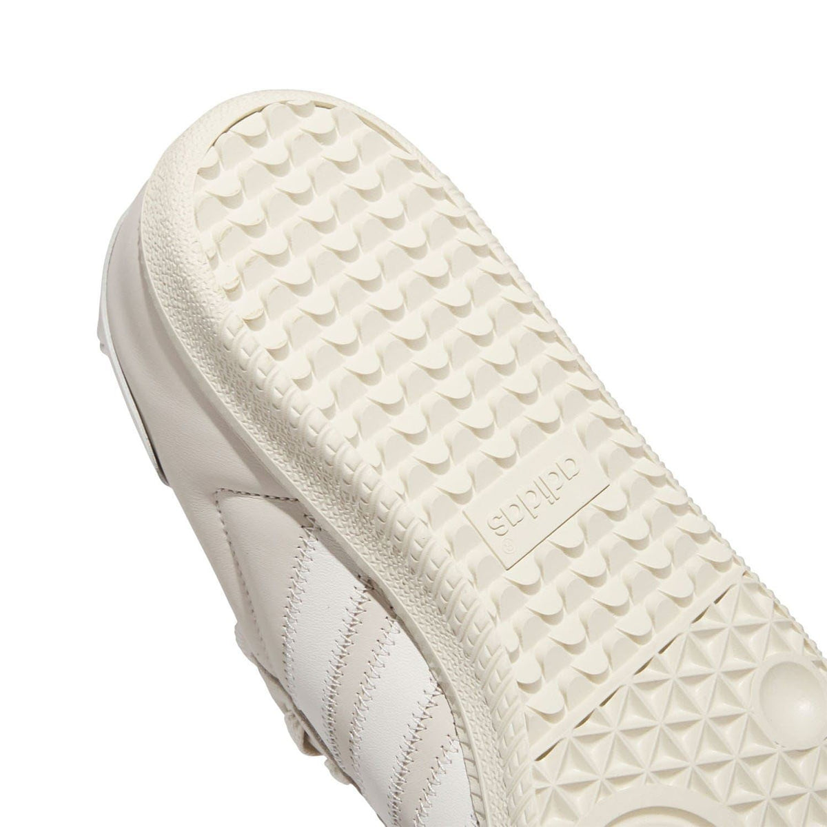 White trainer outsole close-up with geometric tread and embossed lettering