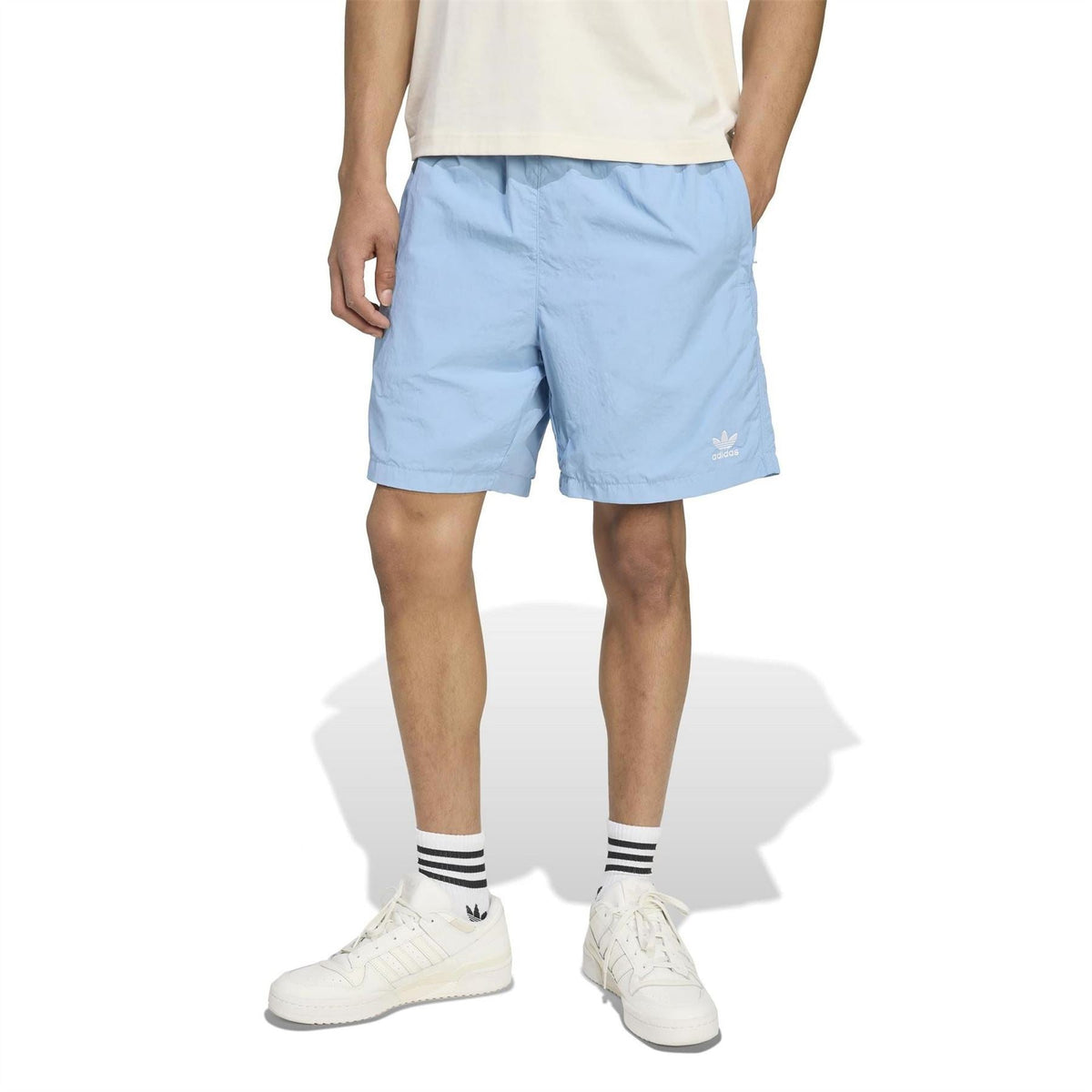Light blue adidas Originals shorts on model, knee-length with adidas logo on hem