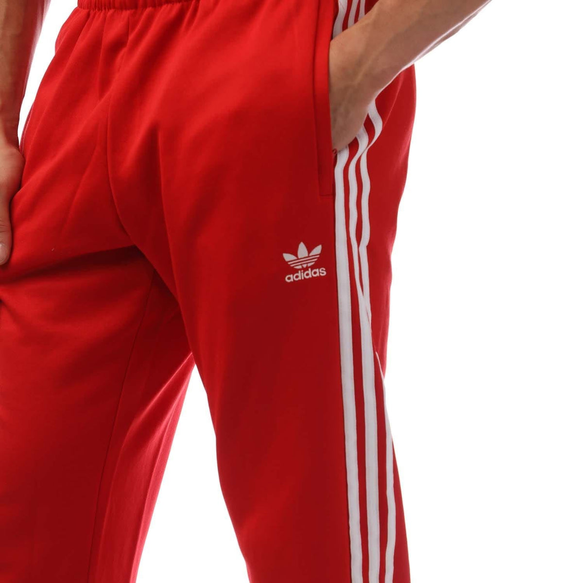 Red adidas track pants with white vertical stripes and trefoil logo on thigh