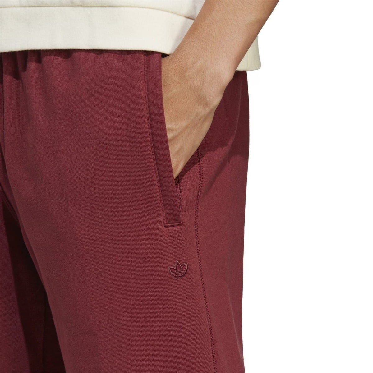 Burgundy track pants detail: side pocket, stitched seams, and adidas trefoil logo