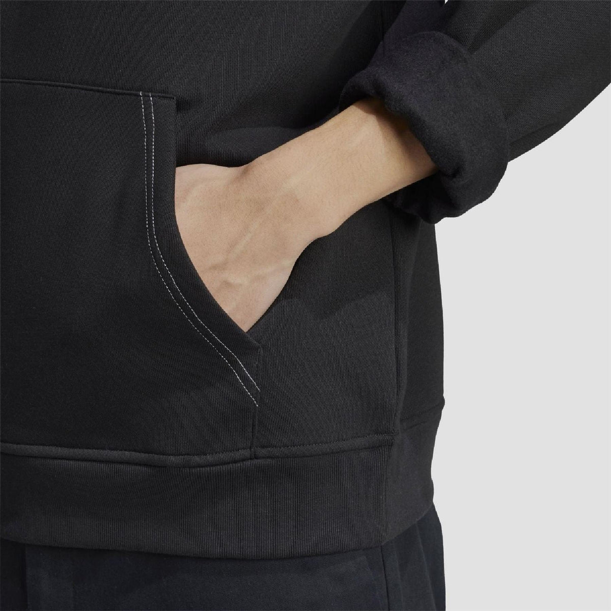 Black hoodie pocket close-up with contrast stitching and ribbed hem cuff