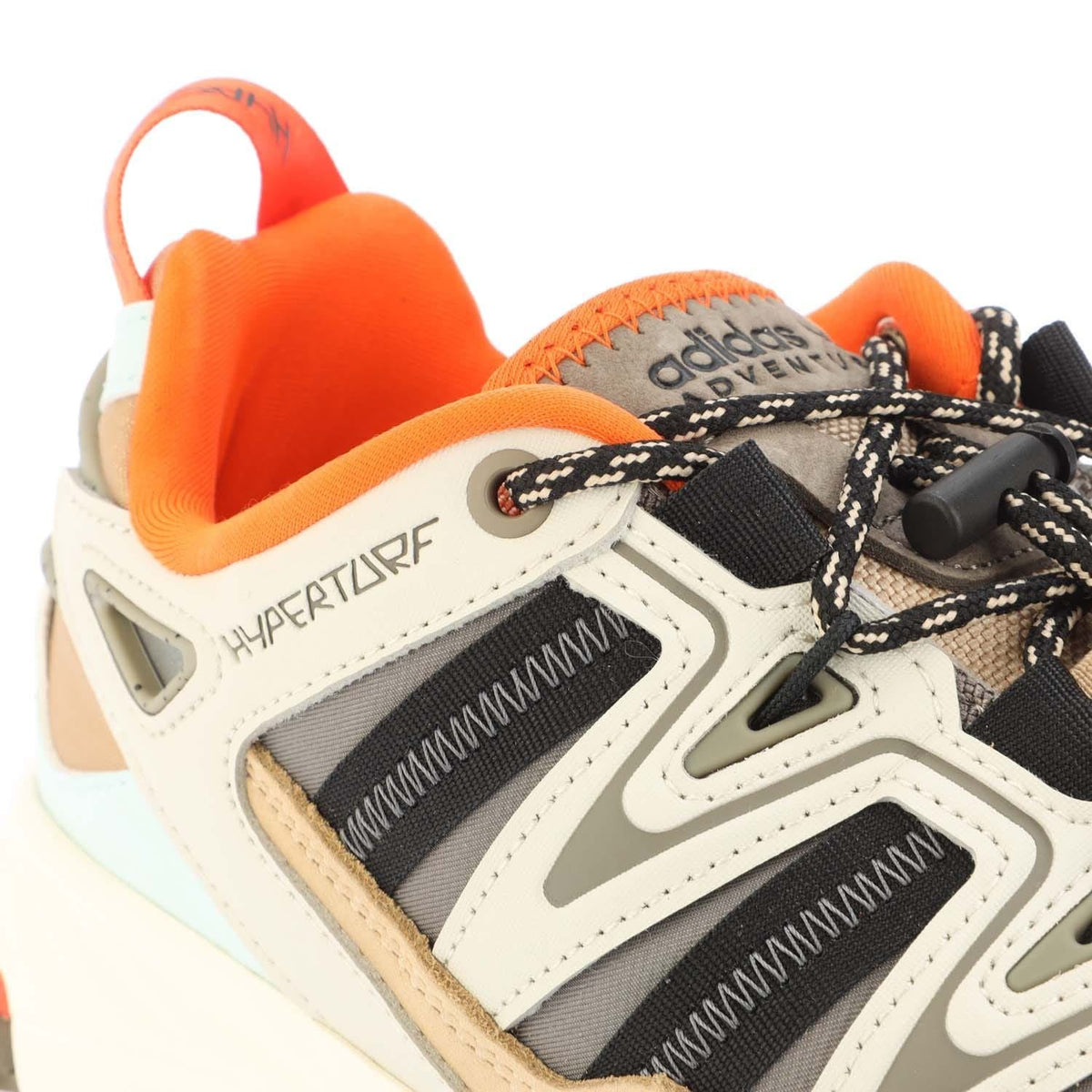 Close-up of cream trainers with black mesh panels, HYPERTURF text, and orange collar
