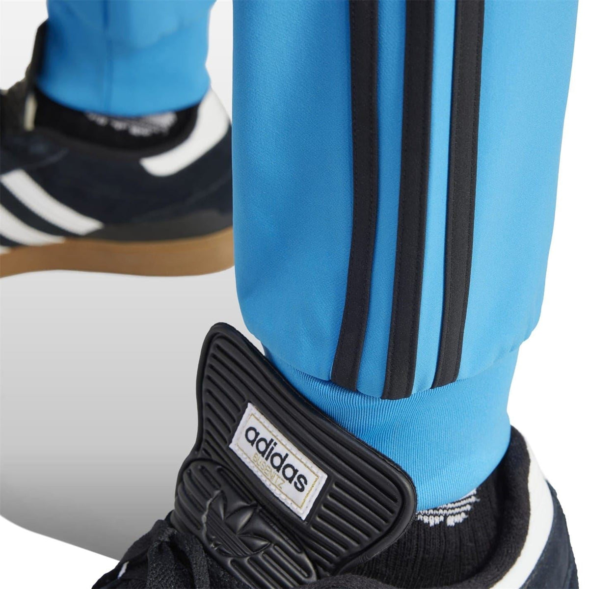 Blue slim track pants with black side stripes and adidas ankle logo