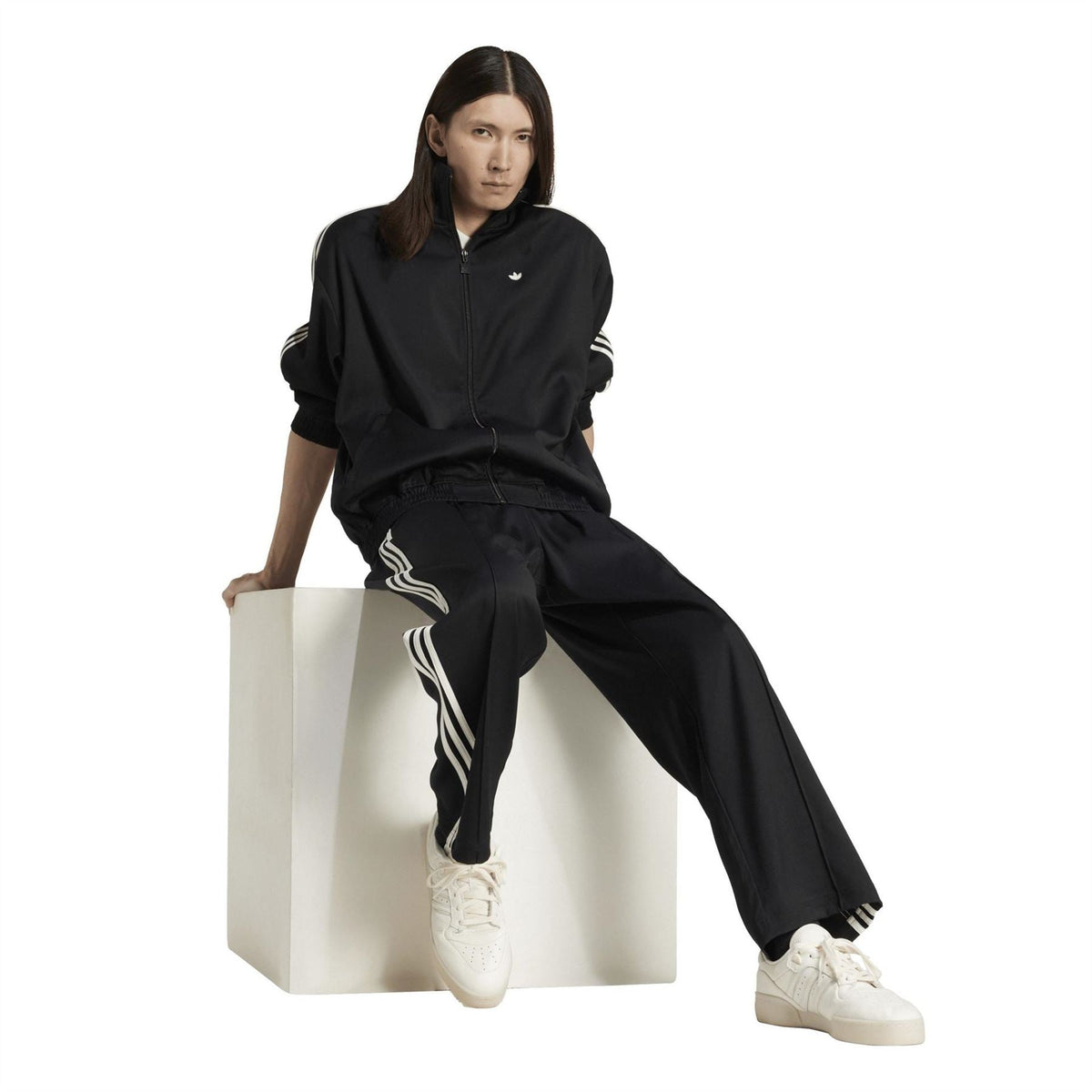 Black adidas Originals track pants with white side stripes, worn with a zip top