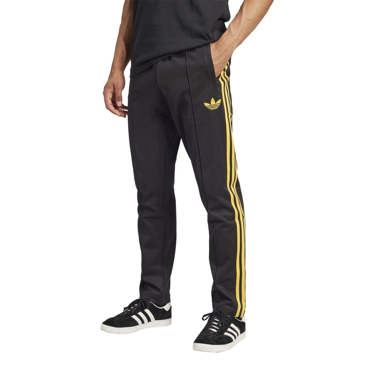 Black track pants with three yellow side stripes, adidas-style trefoil logo, worn with sneakers