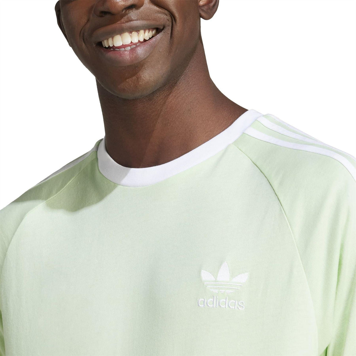 Light green T-shirt close-up: adidas logo and trefoil on chest near crew neckline