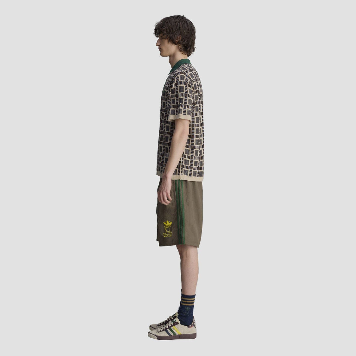 Side view of sand polo shirt; green collar with button placket and navy geometric pattern.