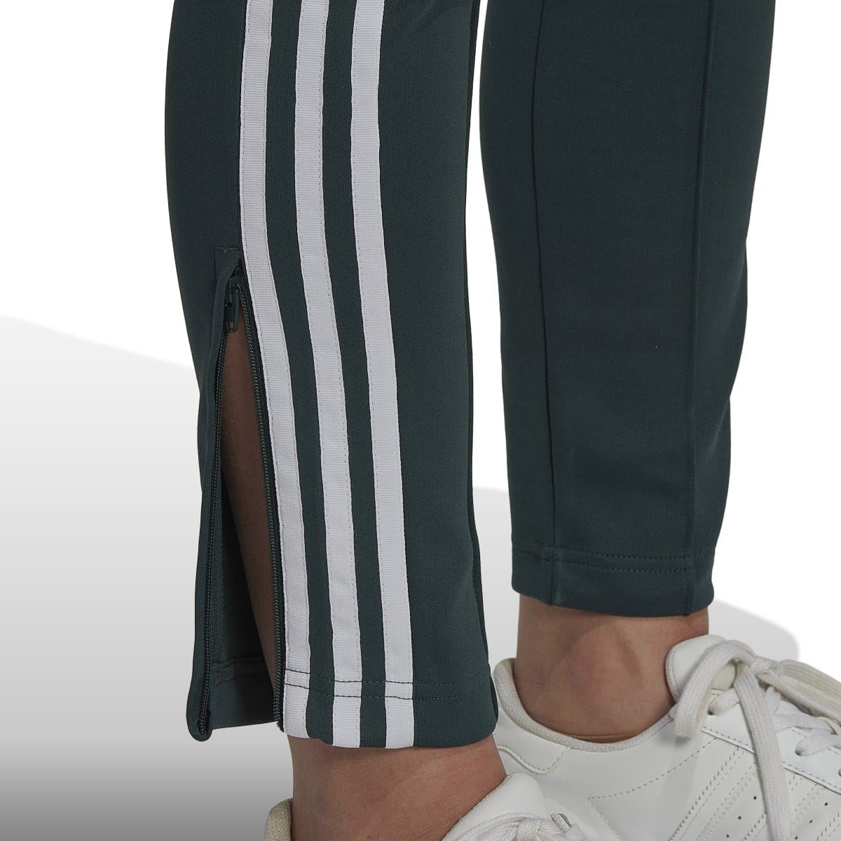 Dark green track pants leg close-up with white triple stripes and ankle cuff