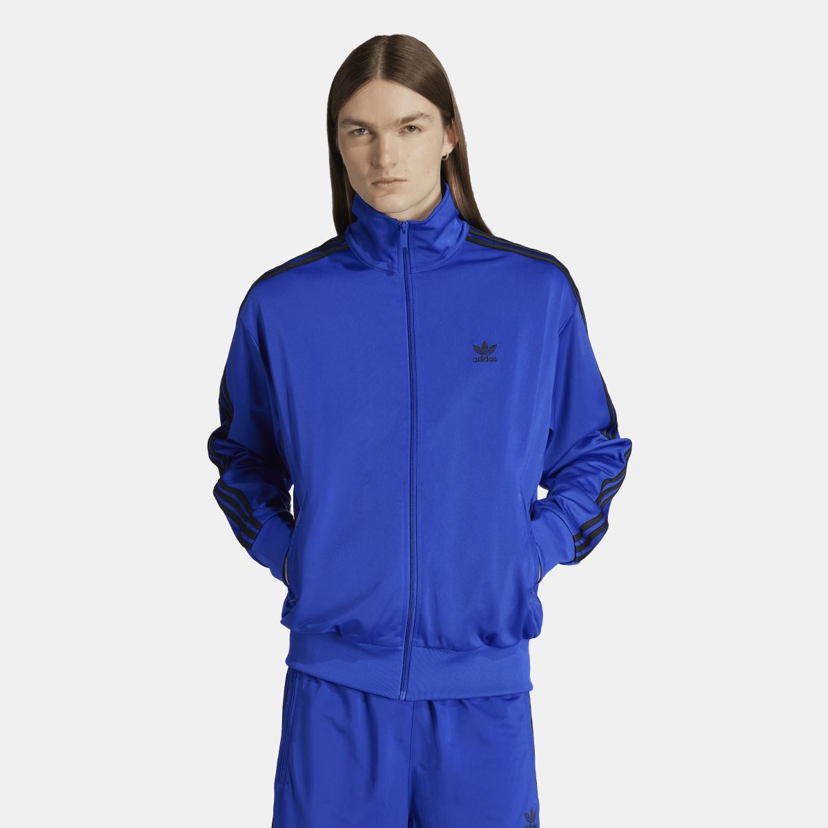 Blue adidas track jacket with full zip and black three-stripe sleeves; model wearing