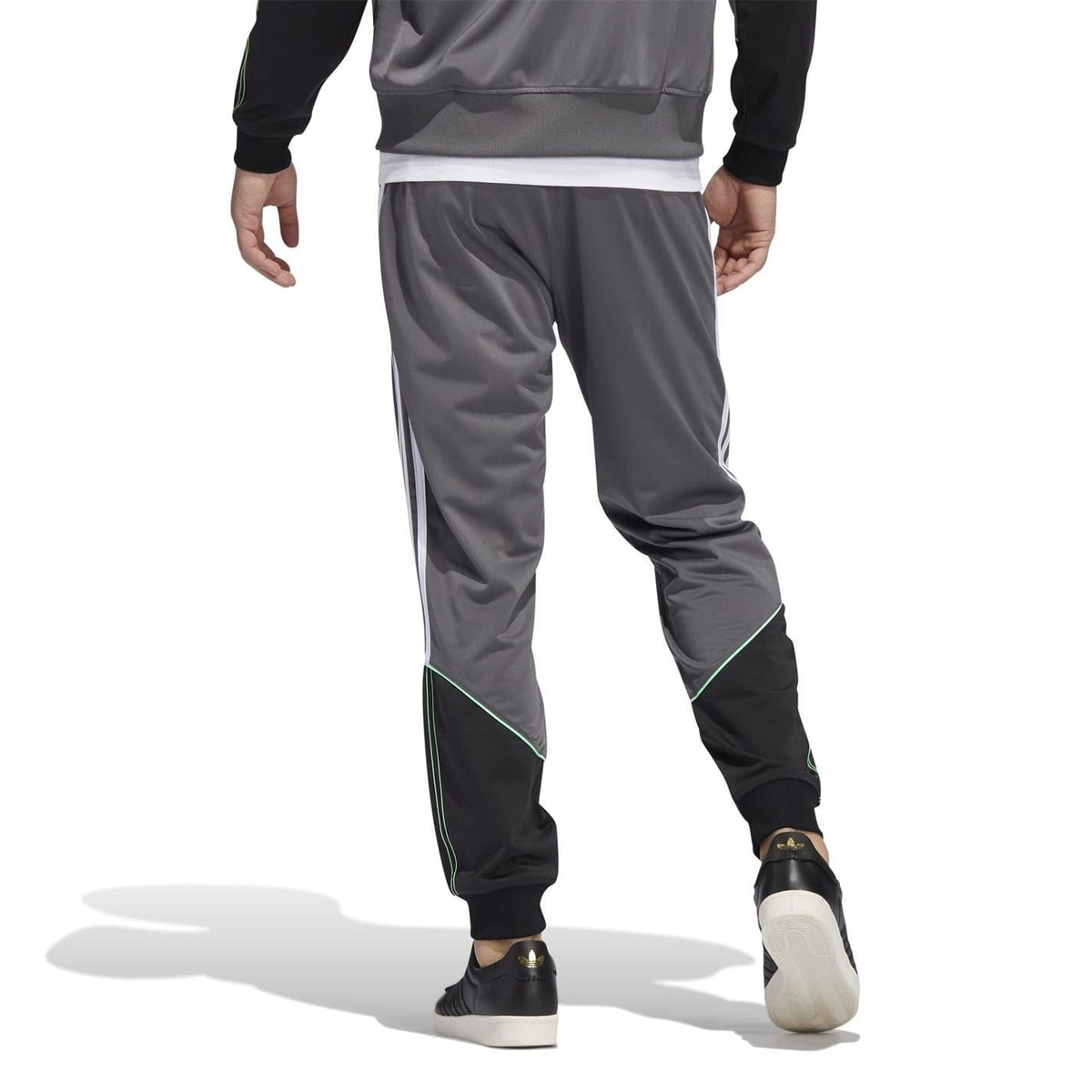 Grey track sweatpants with three white side stripes and green piping at cuffs