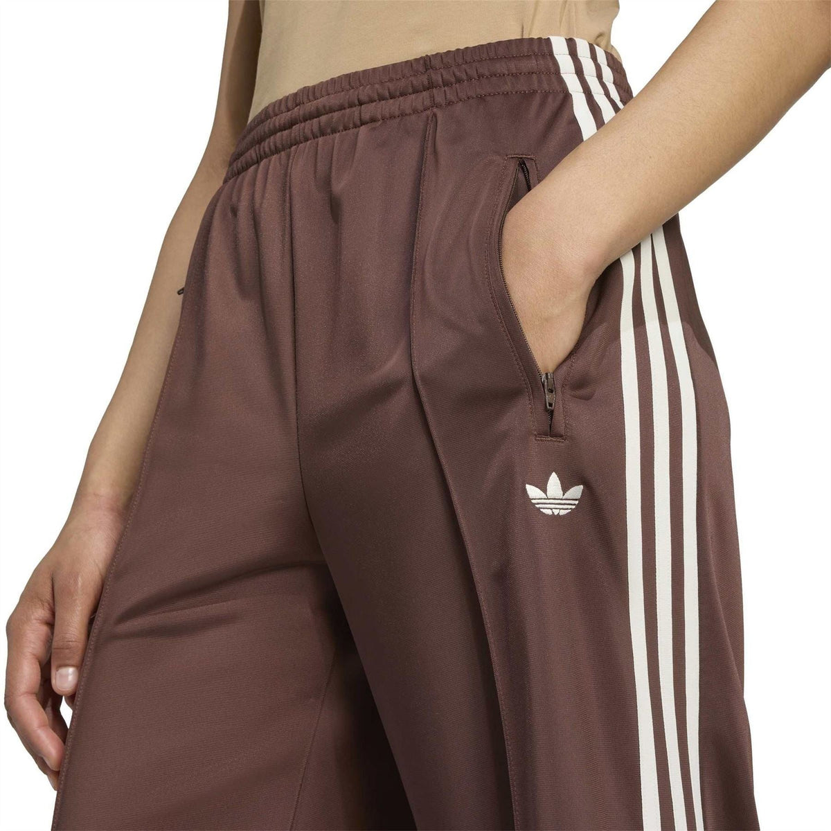 Brown track pants with elastic waistband, front zip, and trefoil logo
