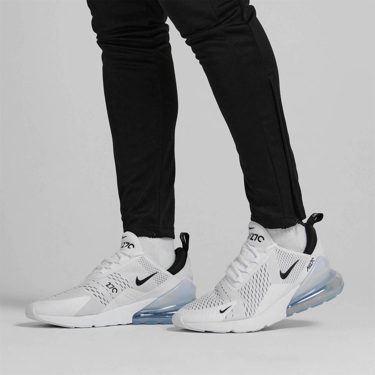 Air Max 270 trainers on feet with black pants; white uppers and light blue air unit
