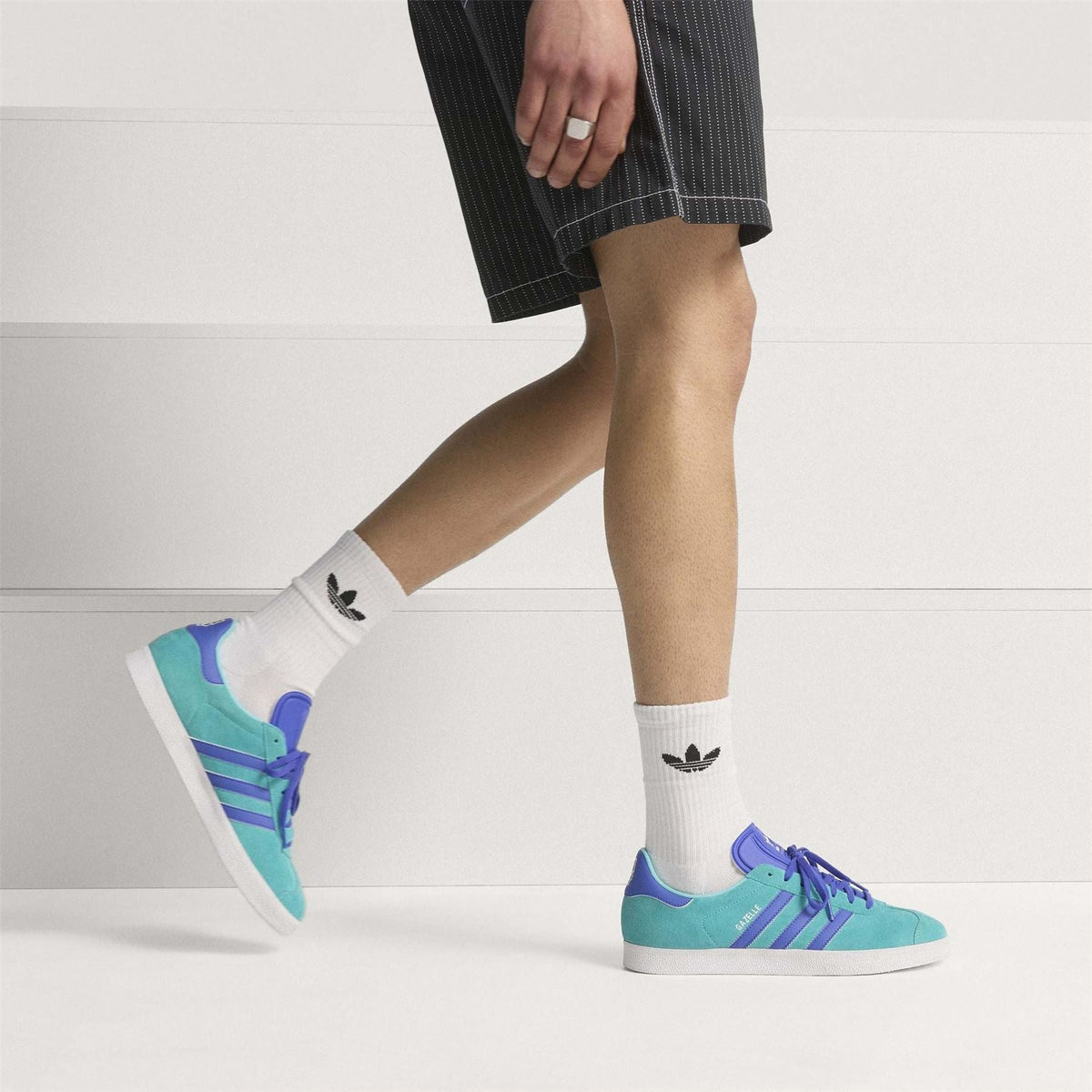 adidas Gazelle suede trainers with teal uppers and purple stripes, worn on feet