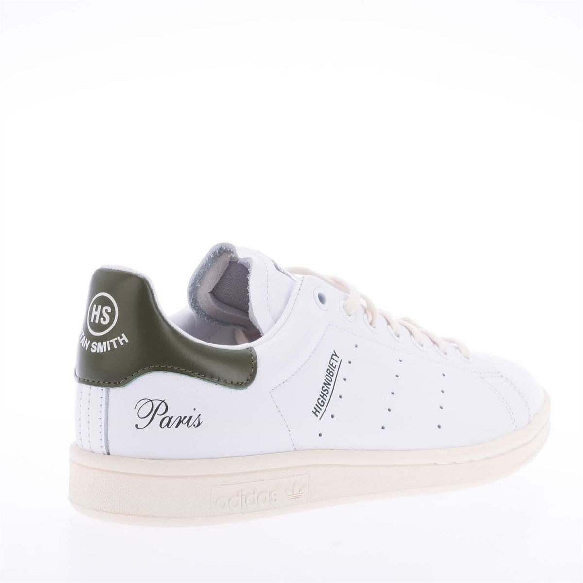White sneaker with green collar lining and “Paris” heel graphic, on beige sole.