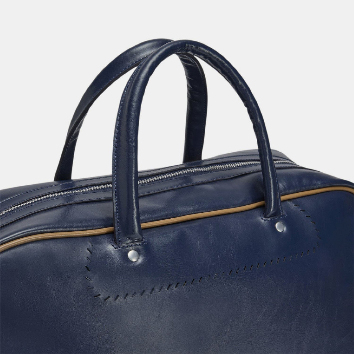 Navy duffel bag front close-up with double zippers and gold trim around handle.