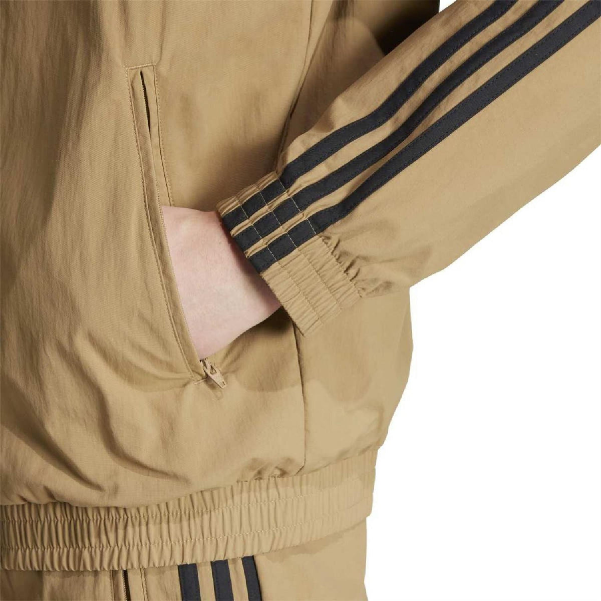 Close-up of tan high-neck track top sleeve cuff and pocket, with navy stripe tape.