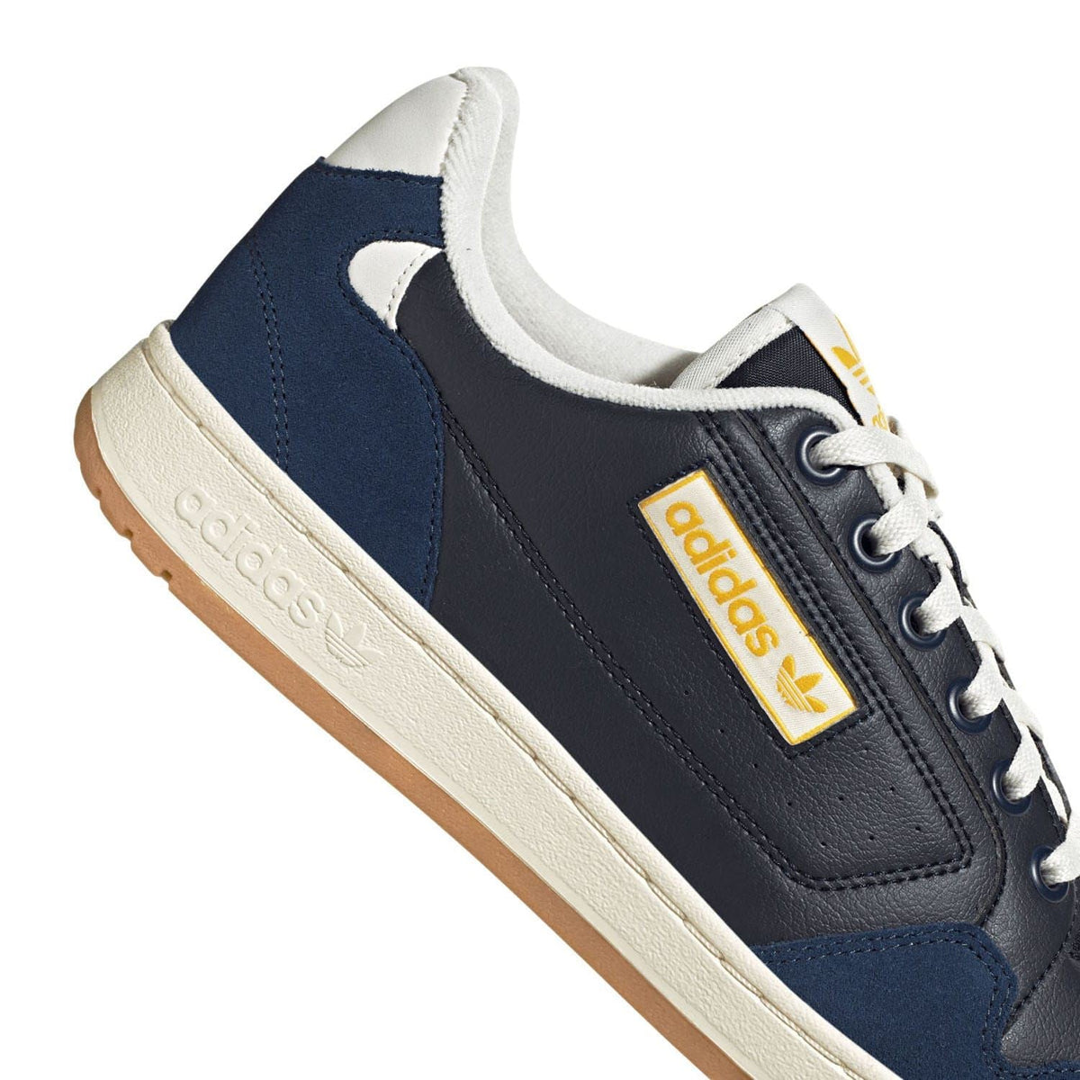 Close-up of navy sneakers with adidas patch, off-white sole, and lace eyelets