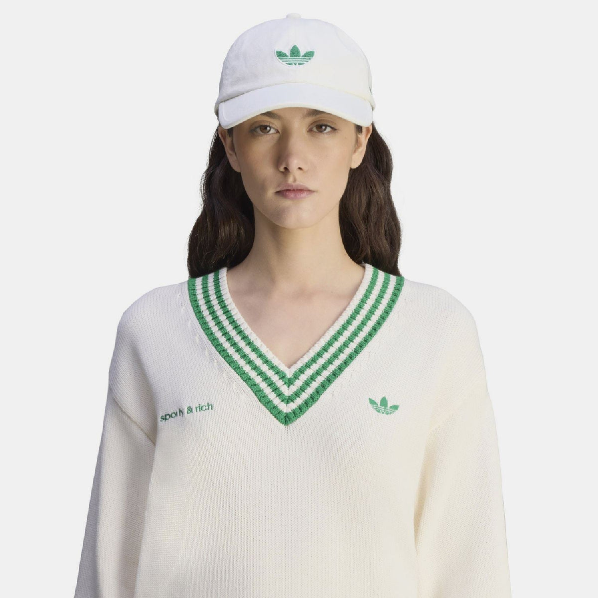 White cap worn by model with green trefoil logo and 'sporty & rich' on front
