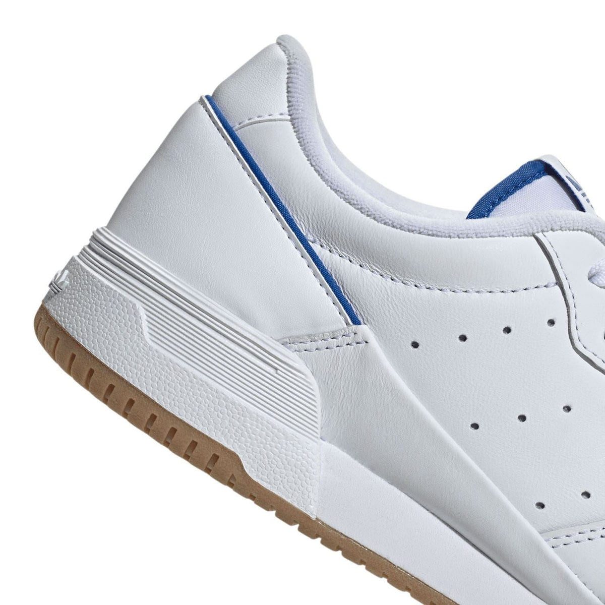 White trainer close-up with blue collar stripe, perforated toe, and lace eyelets.
